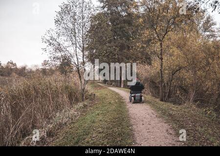 Ein alter Mann fährt mit einem elektrischen Rollstuhl entlang Weg im Herbst Stockfoto