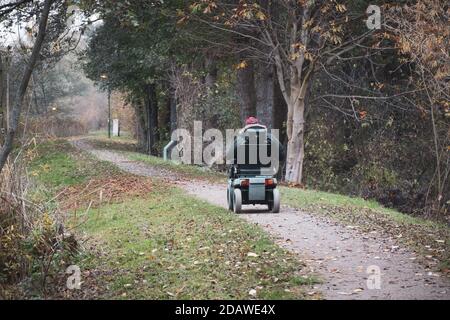 Ein alter Mann fährt mit einem elektrischen Rollstuhl entlang Weg im Herbst Stockfoto