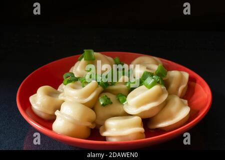 Die Fleischknödel mit Frühlingsanionsen auf schwarzem Hintergrund. Leckeres Abendessen auf rotem Teller auf dem Tisch Stockfoto