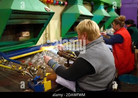 Weibliche Glasbläser blasen Glas blank machen Weihnachtsdekorationen sitzen in Eine Produktionshalle Stockfoto