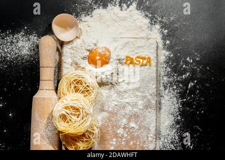 Frisch gekochte Pasta liegt auf einer dunklen, mit Mehl bestäubten Oberfläche. Italienische Pasta. Tagliatelle. Rohe Pasta. Italienische Pasta Rezept. Draufsicht, Kopierbereich Stockfoto