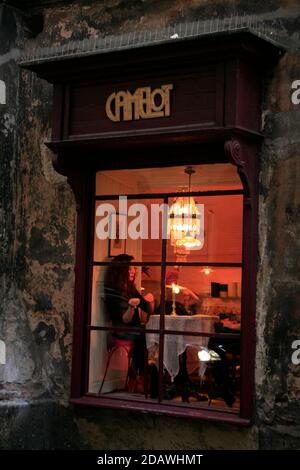 Eine Kundin an einem beleuchteten Fenstertisch, fotografiert von außen im Cafe Camelot, einem bekannten Krakauer Café-Restaurant in der Altstadt. Stockfoto