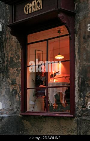 Eine Kundin an einem beleuchteten Fenstertisch, fotografiert von außen im Cafe Camelot, einem bekannten Krakauer Café-Restaurant in der Altstadt. Stockfoto