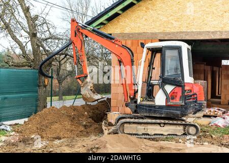 Minibagger auf der Baustelle. Bau eines Familienhauses. Bau eines Wasserversorgungsnetzes. Baustelle mit einem kleinen Bagger. Stockfoto