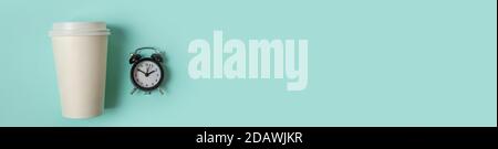 Einfach minimalistisches Design, Papierkaffeetasse und Wecker auf blauem Pastellhintergrund. Getränk zum Mitnehmen und Frühstücksgetränk. Good Morning Wake Up Wake-Konzept. Banner für den Kopierbereich mit flacher Lay-Ansicht von oben Stockfoto