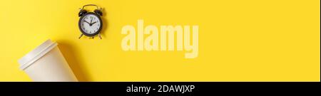 Einfach minimalistisches Design Papier Kaffeetasse und Wecker auf gelb bunten Hintergrund. Getränke zum Mitnehmen und Frühstücksgetränk. Good Morning Wake Up Wake-Konzept. Flach Lay Draufsicht Copy Space Banner Stockfoto