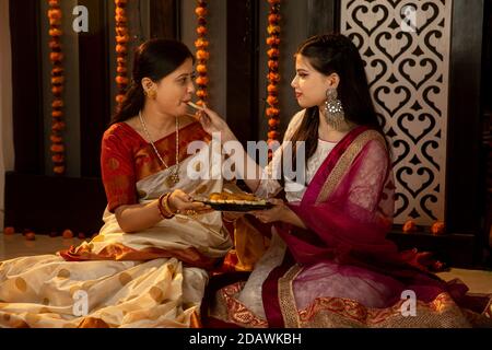 Eine indische Mutter und Tochter feiern das Festival of Lights, indische Familie feiern Diwali. Familie Zeit und zusammen sein. Süßigkeiten teilen. Stockfoto
