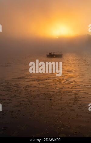 Prairieville, Michigan - EIN schwimmende Floß schwimmt auf Stewart Lake, während die Sonne durch Morgennebel gipfelt. Stockfoto