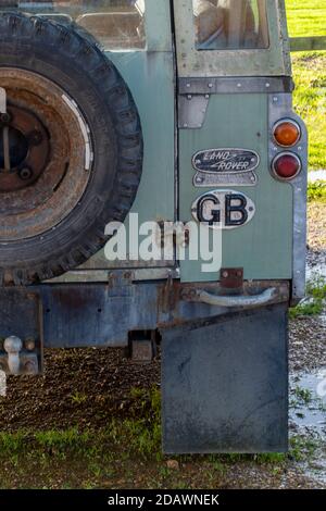 Das Heck eines alten Land Rover mit gb Aufkleber und altmodisches Land Rover Abzeichen neben dem Ersatzteil Radträger Stockfoto