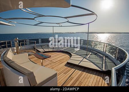 Teak Heck Holzdeck einer großen Luxus-Motoryacht Mit Sonnenliegen, Stühlen, Schlafsofa und tropischem Meerblick im Hintergrund Stockfoto