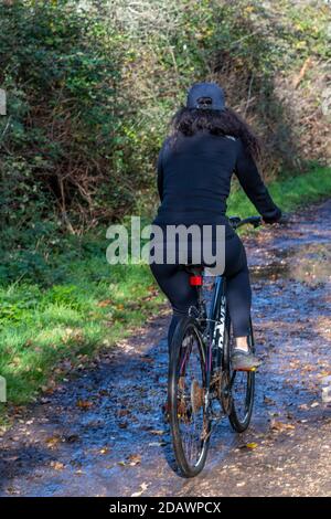 Eine fitte junge Frau in Radbekleidung, die alleine auf einem Landweg im Wald mit dem Fahrrad unterwegs ist. Stockfoto