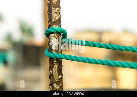 Ein Seil wird in einem Knoten um einen Zaunpfosten gebunden, Seil gebunden Hitch Knoten auf einem rostigen Eisenpol isoliert vom Hintergrund. Stockfoto