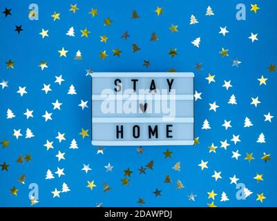 Leuchtkasten mit Stay Home Zitat auf blauem Hintergrund mit Konfetti. Weihnachtsquarantäne. Stockfoto