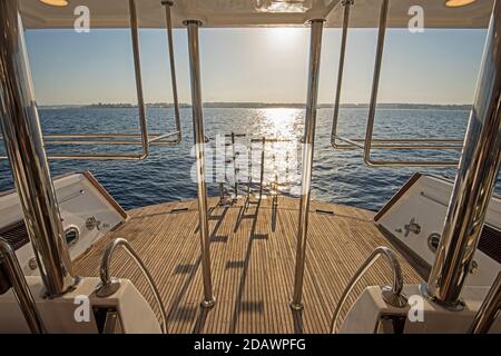 Metallstählerleitern auf der Rückseite Teakholz Deck von A Große Luxus-Motoryacht, die auf einem tropischen Ozean segelt Sonnenuntergang Stockfoto