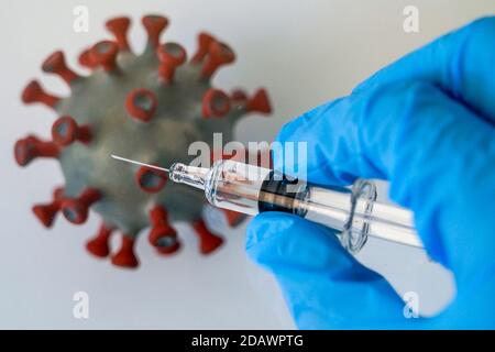 Leipzig, Deutschland. November 2020. ABBILDUNG: Eine Impfspritze wird über ein Modell eines Coronavirus gehalten. Quelle: Peter Endig/dpa-Zentralbild/ZB/dpa/Alamy Live News Stockfoto