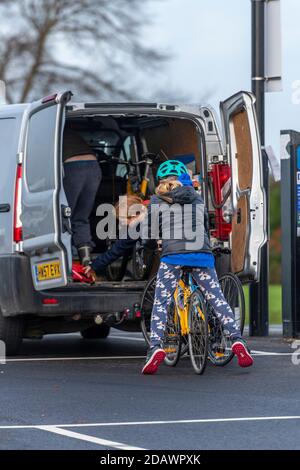 Zwei junge Mädchen warten darauf, dass ihr Vater Fahrräder aus einem Van holen kann, bevor sie auf eine Fahrradtour gehen. Stockfoto