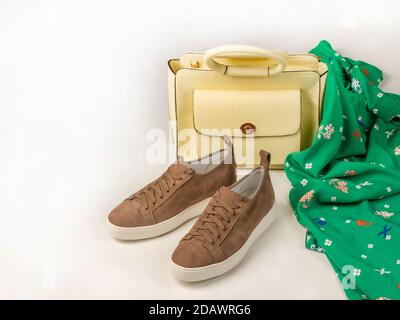 Ein Paar Damen-Sneakers neben einer Tasche aus gelbem Leder und einem grünen Kleid mit stilvollem Druck. Auf weißem Hintergrund. Kopieren Sie den Platz nach links. Stockfoto