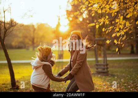 Hallo september. Glückliche moderne Mutter und Tochter in gelben Hüten im Freien auf dem Stadtpark im Herbst Spaß haben Zeit. Stockfoto