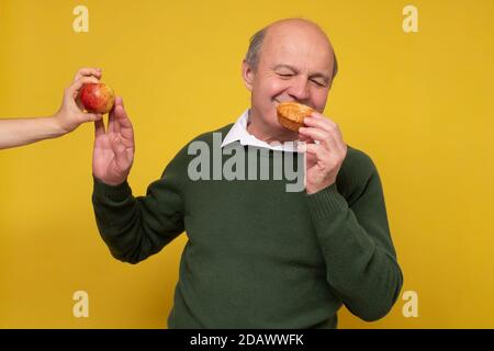 Älterer hispanischer Mann, der sich weigert, Apfel zu essen. Ich esse lieber Kuchen. Stockfoto