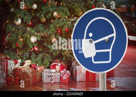 FOTOMONTAGE-Weihafteren 2020 Mitten in der Coronavirus-Pandemie. Wie sieht es mit der teilweisen Sperrung aus? Die Lockerung der Inhaftierten wird wahrscheinlich nur mit deutlich sinkenden Koronazahlen erfolgen. Schildermaskenanforderung vor Weihaftertsbaum, Weihaftertsbaum, Weihnachtsbaum, Weihnachtsbaum, Weihnachtsbaum, geschmückt, Weihnachtsbaumkugel, Geschenke, Pakete. Weltweite Nutzung Stockfoto