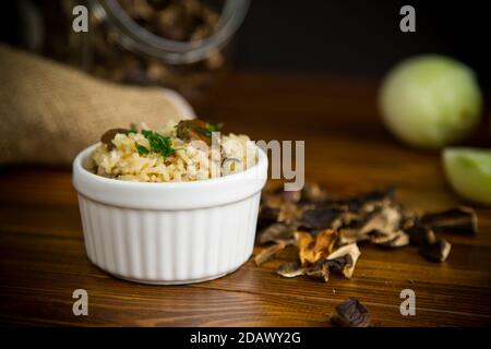 Gekochter Reis mit getrockneten Waldpilzen auf einem Holztisch Stockfoto