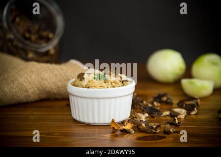 Gekochter Reis mit getrockneten Waldpilzen auf einem Holztisch Stockfoto