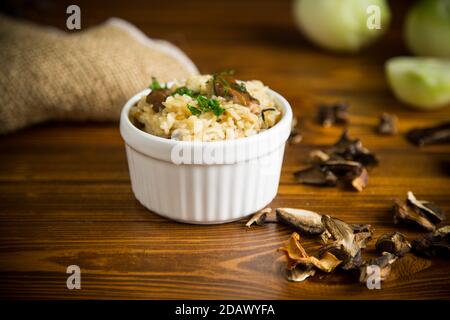 Gekochter Reis mit getrockneten Waldpilzen auf einem Holztisch Stockfoto