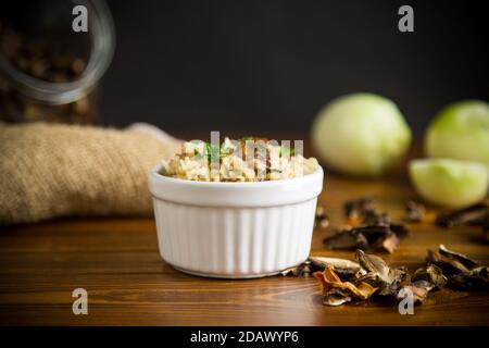 Gekochter Reis mit getrockneten Waldpilzen auf einem Holztisch Stockfoto