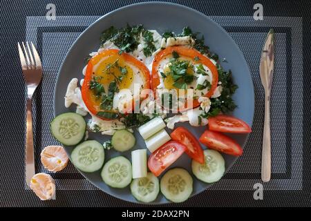 Graue Platte mit Rührei und Gemüse, auf einer grauen Serviette und Mandarinenscheiben nebeneinander. Stockfoto