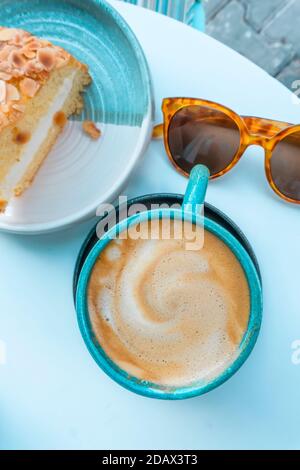 Tasse Cappuccino auf dem Tisch mit Dessert und Sonnenbrille. Mittagessen, Sommer und Erholung in einem Café-Konzept. Stockfoto