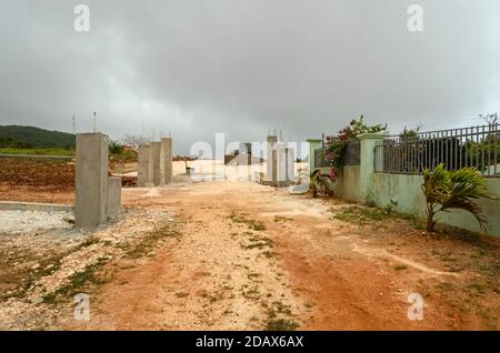 Dunkle Wolken hängen über einer fortschreitenden Straßenbauweise. Entlang der Seiten einer schmalen Straße, die bis zu einem Pflanzenkasten Median führt, auf dem Gelände, sind Säulen Stockfoto