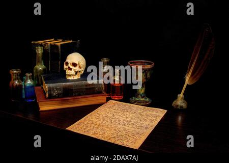 Alter gruseliger Schreibtisch mit Pergament, Federstift, Kelch, Büchern, Totenkopf und Flaschen. Pergament ist nicht zu entziffern Runen. Flaschen haben Farbtränke. Stockfoto