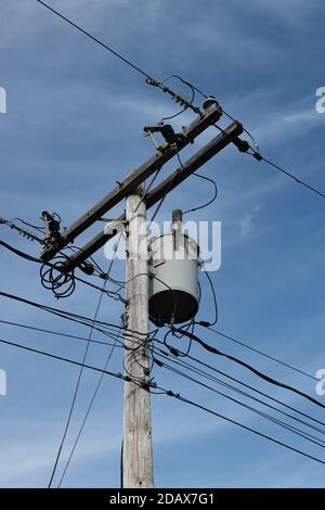 Ein Strommast mit Transformator, Elektro- und Telefonkabeln und Kabel-TV-Kabeln mit blauem Himmel und weißem Wolkenhintergrund. Stockfoto