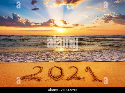 Frohes neues Jahr 2021 kommt Konzept. Nummer 2021 geschrieben am Strand Sand bei Sonnenaufgang. Stockfoto