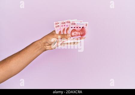 Hispanische Hand mit 100 chinesischen Yuan-Banknoten auf isoliertem rosa Hintergrund. Stockfoto