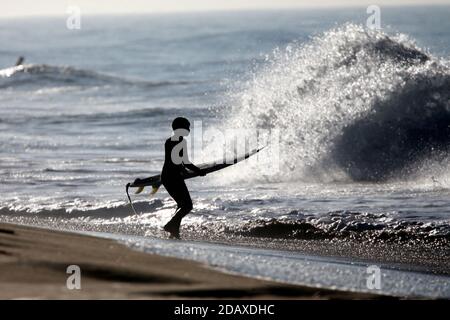 Los Angeles, Kalifornien, USA. November 2020. Ein Surfer mit seinem Surfbrett läuft in Huntington Beach, Kalifornien, Sonntag, 15. November 2020 ins Wasser. Astronomische Hochtiden sind als "King Tides" bekannt und treffen die kalifornische Küste am Sonntag und Montagmorgen, und an einigen Orten bis Dienstag. Kredit: Ringo Chiu/ZUMA Wire/Alamy Live Nachrichten Stockfoto