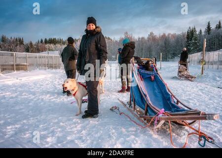 Ziemlich mittleren Alters kaukasischen skandinavischen Frauen hält weißen Husky Hund Vor dem Reiten Hundeschlitten in verschneiten Winter Lappland Landschaft Stockfoto