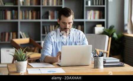 Ein konzentrierter Geschäftsmann sitzt am Arbeitsplatz und arbeitet am Laptop Stockfoto