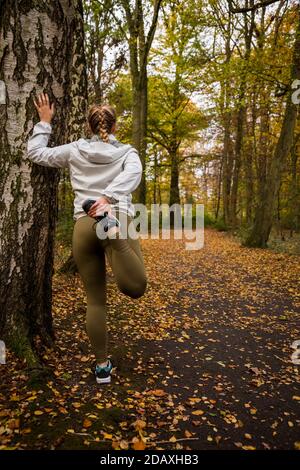 Ein Mädchen, das ihr rechtes Bein neben einem strecken Baum im Wald Stockfoto