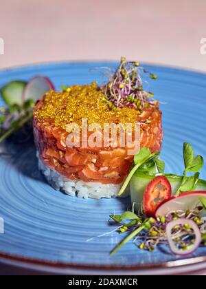 Lachs-Tartare mit goldenem Forellenkaviar auf Reisbasis mit Rettichsprossen. Stockfoto