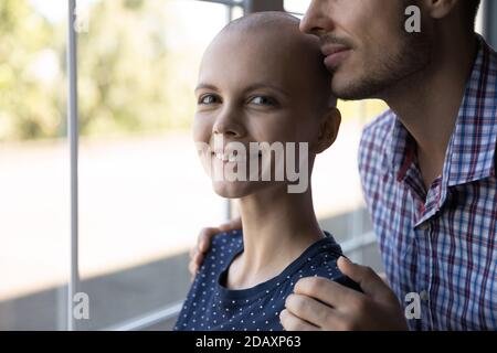 Optimistische junge Frau, die eine Krebsbehandlung erhält, umarmt vom geliebten Mann Stockfoto