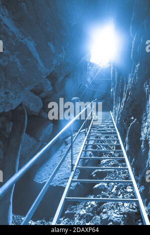 light at the end of the tunnel of a dark cave with ladder Stockfoto