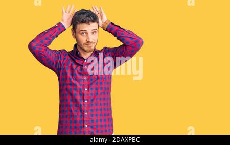 Schöner junger Mann mit Bär trägt Casual Shirt tun Häschen Ohren Geste mit Händen Palmen suchen zynisch und skeptisch. osterkaninchen Konzept. Stockfoto