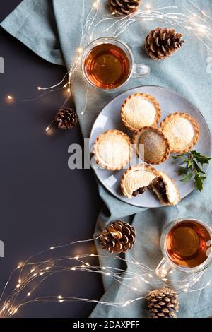 Pasteten auf einem Teller und Tassen mit schwarzem Tee von oben mit Kopierplatz geschossen. Ein Mince Pie ist ein traditioneller Weihnachtskuchen, gefüllt mit einer Mischung aus getrockneten Früchten und Gewürzen Stockfoto