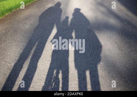 Schatten einer Familie - Mutter, Vater und Kind auf einem Fahrrad - auf einem Spaziergang im Freien im Park Stockfoto