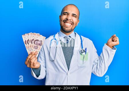 Hispanische Erwachsene Arzt Mann in medizinischer Uniform hält 500 mexikanische Pesos schreien stolz, feiert Sieg und Erfolg sehr aufgeregt mit angehoben Stockfoto