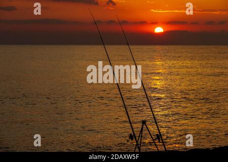Vorderansicht des Meeres Sonnenuntergang im Vordergrund zwei Angelruten und im Hintergrund das Meer und die Untergehende Sonne Stockfoto