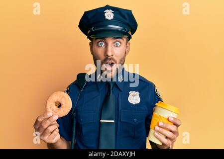 Gutaussehende hispanische Polizei Mann essen Donut und trinken Kaffee Angst und schockiert mit Überraschung und erstaunt Ausdruck, Angst und aufgeregt Gesicht. Stockfoto