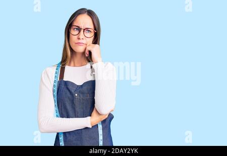 Schöne Brünette junge Frau Schneiderin Designer tragen Atelier Schürze ernstes Gesicht Denken über Frage mit Hand auf Kinn, nachdenklich über conf Stockfoto