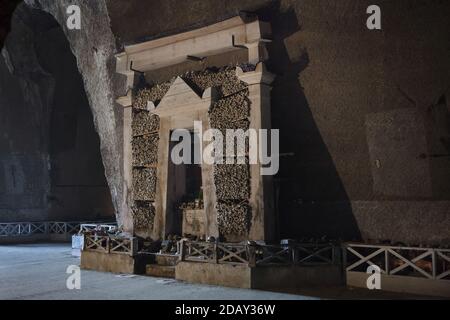 Seitenaltar aus gestapelten menschlichen Knochen im Friedhof Fontanelle (Cimitero delle Fontanelle) in Neapel, Kampanien, Italien. Das ehemalige Leichenhaus (Beinhaus) in einer Höhle im Stadtteil Materdei war der Ort, an dem sich in Neapel der spontane Kult der Hingabe an die Überreste namenlos Verstorbener entwickelte. Die Verteidiger des Kults besuchten die namenlosen Schädel im Beinhaus, um sie zu adoptieren und den Schädeln sogar Namen zu geben. Adoptierte Schädel wurden in der dekorierten Box platziert und wurden zum Gegenstand des regelmäßigen Gebets und Votivopfers. Stockfoto